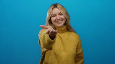 Sarı süveter giymiş, mavi arka planda gülümseyen bir kadın, sarı saçlı, beyaz tenli, davetkar bir şekilde el ele tutuşan, neşeli ve sakin bir ortam..