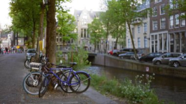 Amsterdam 'da bir kanal boyunca park etmiş bisiklet tarihi binaları ve şehir yaşamını gösteren bulanık bir arka plan Hollanda' da huzurlu ve resimsel bir bokeh etkisi yaratıyor..