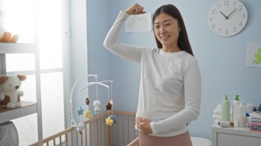 Bebek beşiğinin yanındaki rahat bir yatak odasında kendine güvenen bir kadın neşeli bir yüz ifadesi sergiliyor. Parlak bir iç mekan, hoş geldin atmosferini vurguluyor..