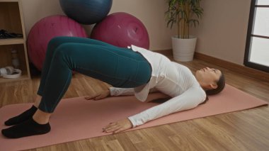 Spor salonunda spor salonunda spor yapan kadın briç oynarken etrafını spor aletleriyle donatarak spor yapıyor.