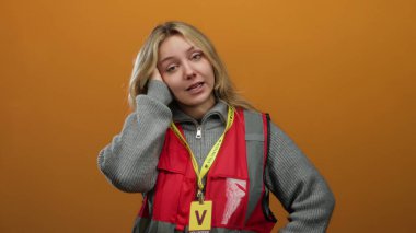 İzole edilmiş turuncu arka planda kırmızı yelek giyen genç gönüllü kadın düşünceli görünüyor..