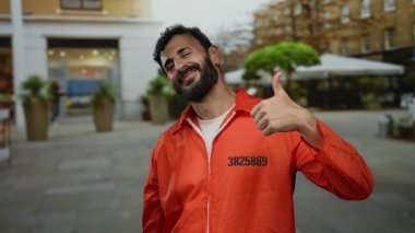 Sakallı ve turuncu tulumlu İspanyol bir adam sokakta dikiliyor, neşeli hareketler sergiliyor ve arkadaşlığını ifade ediyor..