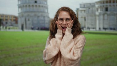 İtalya 'da sidik kulesinin yanında gülümseyen genç bir kadın, açık havada güneş gözlüğü ve süveter takıyor, Avrupa mimarisini ve neşeli seyahat atmosferini yakalıyor..