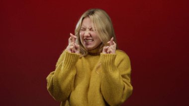 Kırmızı arka planda umut verici bir ifadeyle, sarı kazak giyen bir kadın, beklenti anını yakalıyor..