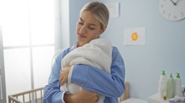 Yatak odasında bebeğini kucağında tutan kadın mutlu ve huzurlu görünüyor. Arka planda beşiği olan yumuşak sabah ışığına karşı..