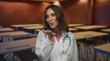 Steteskoplu beyaz önlüklü doktor sınıf ortamında öpücük yolluyor, bakımı ve eğitimi simgeliyor..