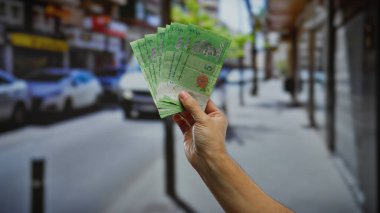 Kentsel bir sokak ortamında el ele tutuşan Malezya bankası banknotları, bir şehir ortamında ticari işlemleri ve döviz alışverişini gösteriyor.