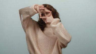 Elleri rahat bir süveter içinde hayali bir fotoğrafı arka planda gösteren bir kadın. Yaratıcılığı ve oyunculuğu eğlenceli bir jestle ifade ediyor..