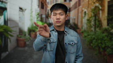 Genç Çinli bir adam canlı bir şehir caddesinde kot ceket giyerek jest yapıyor, açık hava ortamında sıradan bir şehir yaşam tarzını çağrıştırıyor..