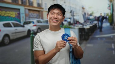Elinde mavi kurdele tutan Asyalı genç adam canlı bir şehir caddesinde park etmiş arabaları ve açık hava yemekleriyle dururken gülümsüyor, başarıyı ve şehir yaşam tarzını somutlaştırıyor..