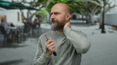 Şehir sokağında elinde bulmaca gibi bir ifadeyle arabanın anahtarlarını tutan, gri bir kazak giyen, bulanık şehir arka planıyla çevrili, merak ve düşüncenin uyandıran bir adam..