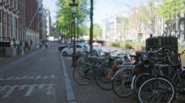 Bulanık bisiklet manzarası Amsterdam Kanal Caddesi 'nde insanlarla ve klasik mimariyle iç içe. Hollanda' da hayat dolu şehir hayatı ve seyahat izlenimi uyandırıyor..