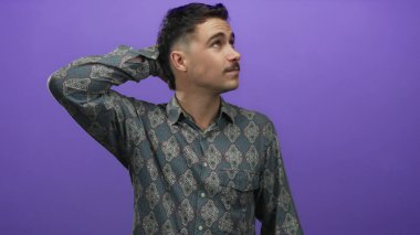 Şablonlu tişörtlü genç İspanyol bir adam, düşünceli bir şekilde kafasını soyutlanmış bir mor arka plana sürtüyor, tefekkür ve iç gözlem yapıyor..