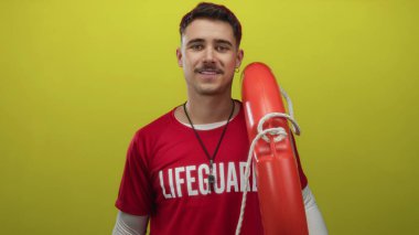 Genç İspanyol cankurtaran, izole edilmiş sarı arka planda kırmızı şamandıra tutuyor.