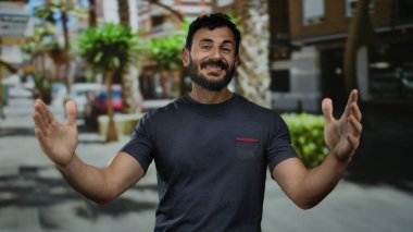 Sakallı İspanyol bir adam şehir caddesinde ağaçlar ve binalar arkasında mutluluk ve kendine güveni ifade ederek neşeli bir şekilde dolaşır..