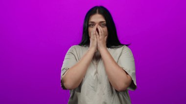 Uzun siyah saçları ve anlamlı gözleri ile endişeli görünen bir kadın, izole pembe arka plan karşısında duruyor, elleri göğsüne dokunuyor endişe içinde..