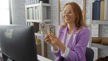 Ofis masasında içi kitap ve belgelerle dolu bir bilgisayar ve rafla para sayan, gülümseyen ve işine odaklanmış, şık gözlükler takan ve spor ceket giyen bir kadın..