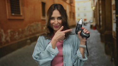 Bir kadın, elinde bir sokak matkabı tutarken gülümsüyor. Açık havada kentsel manzarayla çevrili, İspanyol asıllı genç bir şahıs sergiliyor..