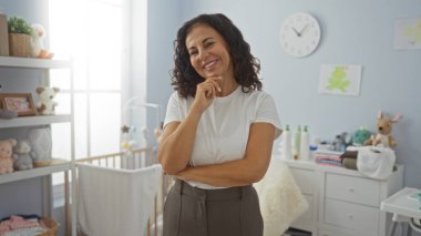 Yatak odasında beşikte oyuncaklarla ve dekorla çevrili gülümseyen bir kadın ev ortamını yansıtıyor, mutluluğunu ve sıcaklığını gösteriyor..