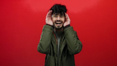 Elleri kırmızı arka planda, yeşil ceketli genç adam çeşitli duyguları canlı bir şekilde ifade ediyor.