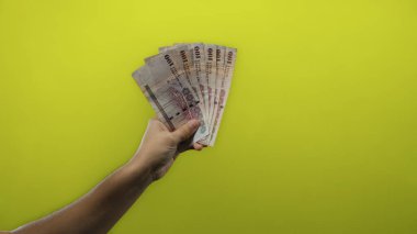 Suudi Arabistan 'ın riyal banknotlarını tutan adam, parlak sarı arka plana uzanan, para ve finans temasını yakalayan,.