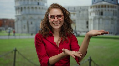 Gülümseyen kadın, İtalya 'da sidik kulesinin yanında elini uzatıyor. Kırmızı tişörtlü, açık havada güneşli bir gün portresi gözlüğü takıyor. Turist çekimleri canlanıyor..