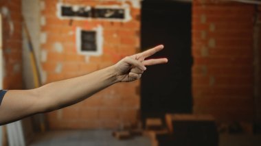 Duvarın arka planında bulanık tuğlalar olan bir inşaat alanında el hareketleriyle ev ortamında umut ve dönüşüm kavramlarını vurgulayan bir adam..