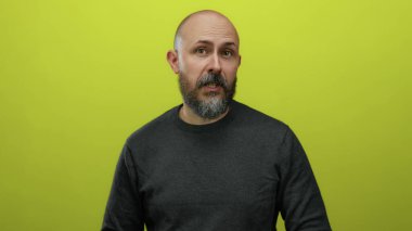 Sakallı, beyaz, kel bir adam. Sarı arka planda duruyor. Düşünceli ve anlamlı görünüyor..