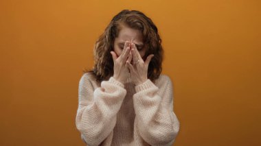 Elleri rahat bir kazakla yüzünü örten kadın canlı turuncu arka planda duygularını ve içsel gözlemlerini izole bir ortamda aktarıyor..