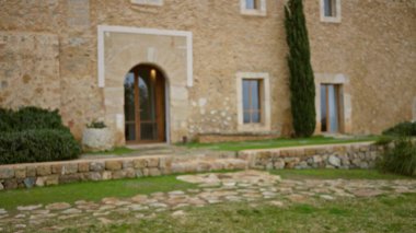 Taş duvarları ve kemerli kapıları olan eski bir Akdeniz evinin bulanık manzarası. Etrafı yeşilliklerle çevrili. Sakin bir ortamda, kırsal bir mimari sergileniyor..