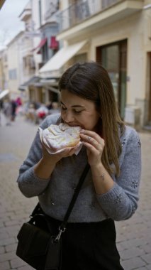 Eski şehrin sevimli bir caddesinde geleneksel hamur işiyle eğlenen bir kadın genç ve neşeli bir atmosferle canlı bir açık deniz manzarası yakalıyor..