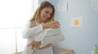 Sıcak yatak odasında, bebeğini kucağında tutan bir kadın, beşikteki yumuşak doğal ışık altında, sessiz bir evde bebekle sıcak bir annelik bağı kuruyor..