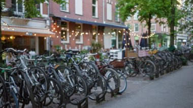 Bisikletler bulanık bir arka plan ve bokeh ışıkları ile Amsterdam caddesinde dizilmiş, canlı şehir atmosferini ve günlük açık hava yemeklerini yakalıyorlar..