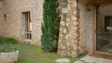 Eski bir Akdeniz taş evinin dış görünüşü bulanık. Odaklanamayan yeşil bitkiler ve kırsal elementler açık havada atmosferik bir çukur oluşturuyor..