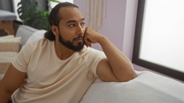 Sakallı genç adam, modern apartman odasının iç tarafındaki kanepede rahatlıyor..