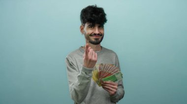 İzole edilmiş mavi arka plana karşı Norveçli kronu tutan adam, servetini güvenle gösteriyor.