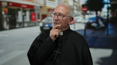 Düşünceli bir ifadeye sahip yaşlı bir rahip bulanık şehir geçmişiyle hareketli bir caddede duruyor ve sakin tavırlarına ve inancına yansıyor..