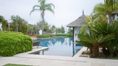 Dışardaki tropikal lüks bir tatil köyü, çözünmüş palmiye ağaçları, bokeh tarzı havuz, yemyeşil, dingin ve egzotik bir tatil ortamını çağrıştırıyor..