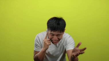 Genç Çinli adam telefonda izole edilmiş sarı duvar arkasına karşı konuşuyor. Güçlü duygular sergiliyor..