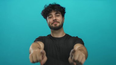 Sakallı, gülümseyen ve mavi arka planda kameraya bakan genç bir İspanyol, davetkar bir ortam yaratıyor..