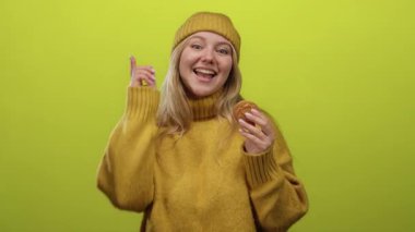 Elinde kurabiyeyle gülümseyen ve parlak yeşil arka planda kameraya bakan bir kadın..