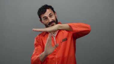 Turuncu tulumlu İspanyol bir adam gri arka planlı bir hapishane ortamında mola jesti yapıyor..