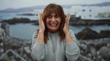 Deniz kenarındaki sahilde duygularını ifade eden kıdemli İspanyol kadın. Açık havada bulanık bir okyanus geçmişi var..