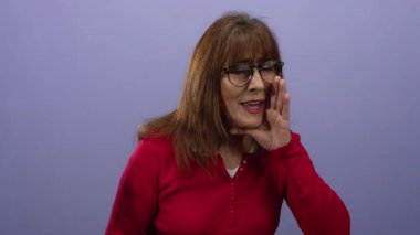 Kırmızı kazaklı kadın mor duvara yaslanmış. Yüzünde bir eliyle yüksek sesle konuşuyor. Gözlük takıyor ve anlamlı bir jest yapıyor..