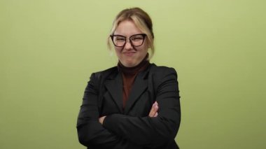 Gözlüklü bir kadın yeşil bir arka plana karşı komik yüzler yapıyor, siyah ceket ve kahverengi balıkçı yaka giyiyor, çeşitli şakacı ifadeler sergiliyor kolları çapraz veya jest ile.