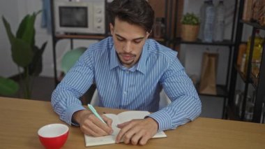 Kapalı ofis ortamında günlük ambiyans, mavi çizgili gömlek, beyaz bardak ve profesyonel atmosferi geliştiren modern mobilyalar gibi şeyler yazan genç bir adam..