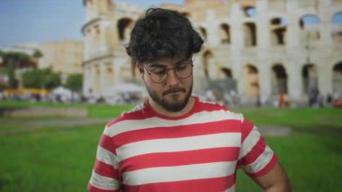 Sakallı ve gözlüklü genç adam güneşli bir günde Roma kolezyumunda dikiliyor..
