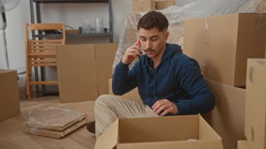 Yeni evdeki İspanyol genç adam. Etrafı kutularla çevrili. Oturma odasında telefonla konuşuyor.