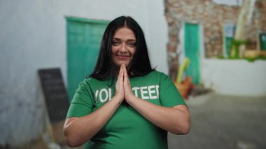 Yeşil tişörtlü gönüllü bir kadın güneşli gökyüzünün altında şehir sokaklarında huzur içinde gülümsüyor..