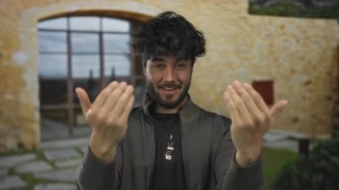 Kırsal kesimde güneşli bir günde neşeli bir şekilde el kol hareketi yapan sakallı genç bir adam mutluluk ve canlılık sergiliyor..